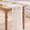 A semi-sheer white gauze table runner is draped over a wooden table, set for a meal.