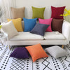 A collection of colorful linen pillows in shades of yellow, green, blue, pink, and terracotta arranged on a white sofa.