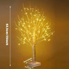 A tall, slender birch tree decorated with warm yellow LED lights on a white base.