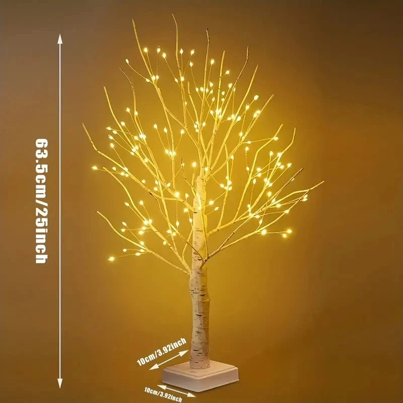 A tall, slender birch tree decorated with warm yellow LED lights on a white base.