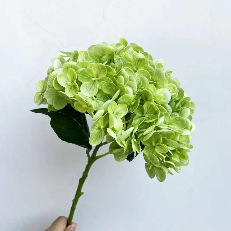 A vibrant light green artificial hydrangea bouquet with dark green leaves.