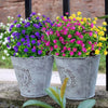Two galvanized pots filled with vibrant faux floral plants featuring purple, pink, and yellow blooms.