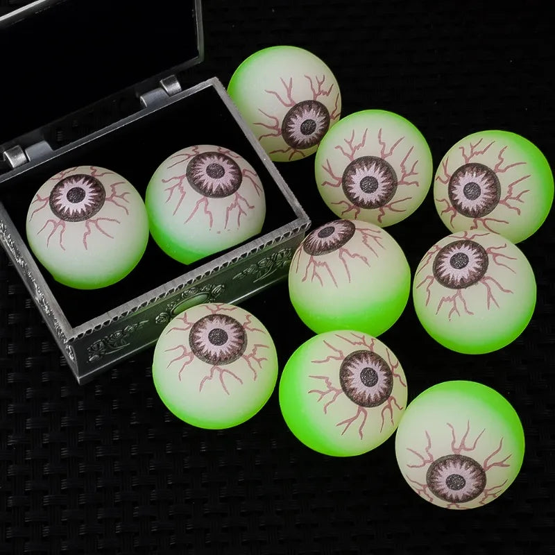 A collection of glow-in-the-dark eyeball bouncy balls in various shades of green and white resting in a clear box.