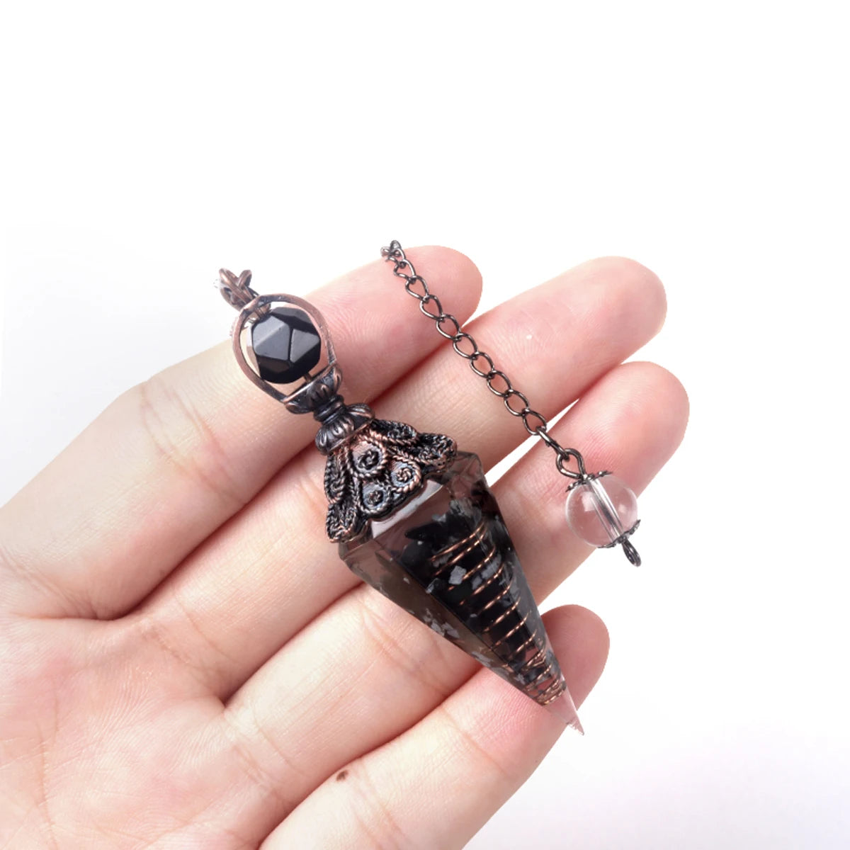 A hand holds a natural crystal pendulum necklace set featuring a dark, pointed crystal pendant and a silver chain.