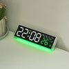 A digital LED alarm clock displaying 22:08 and 26 degrees with a green ambient light on a white surface.
