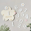 A collection of wooden monthly milestone cards featuring numbers and flowers on a light gray background.