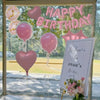 A window display featuring pink balloons and a banner that reads Happy Birthday for a party.