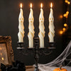A set of four white, elongated soy candles shaped like ghosts or mummies displayed on an antique iron candelabra.