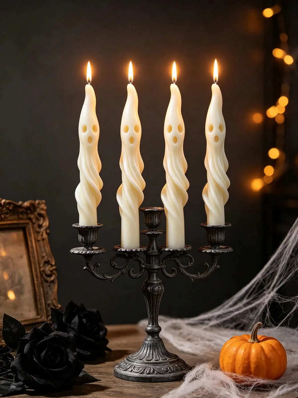 A set of four white, elongated soy candles shaped like ghosts or mummies displayed on an antique iron candelabra.