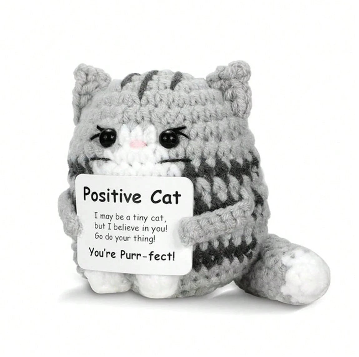 A handmade gray and white crochet mini cat plush with a sign that reads You're Purr-fect