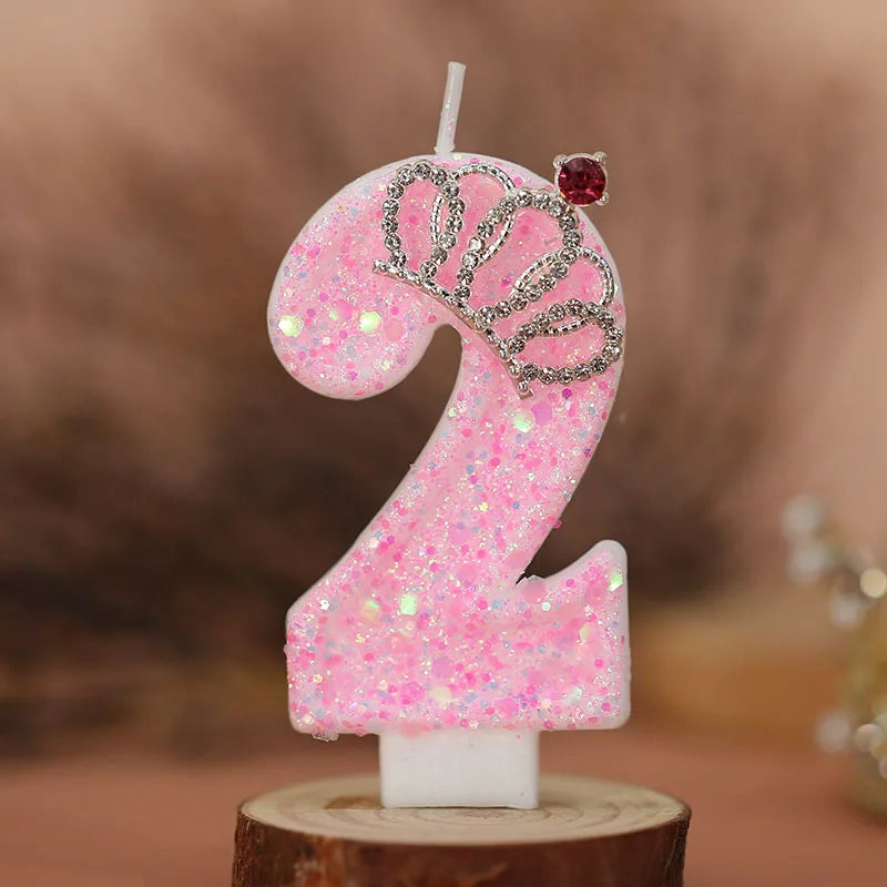 Pink glitter number two birthday candle with a silver crown topper on a wooden base