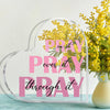 A clear acrylic heart-shaped sign with the text Pray it over it pray through it overlaid on a background of yellow flowers.