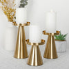 A set of three elegant gold metal candle holders with white pillar candles on a light gray surface.