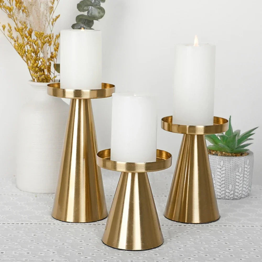 A set of three elegant gold metal candle holders with white pillar candles on a light gray surface.