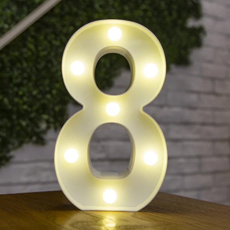 A glowing warm white LED alphabet letter light shaped like the number eight resting on a wooden surface.