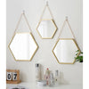 A hexagon decorative wall mirror with a gold frame and hanging on a light gray wall.