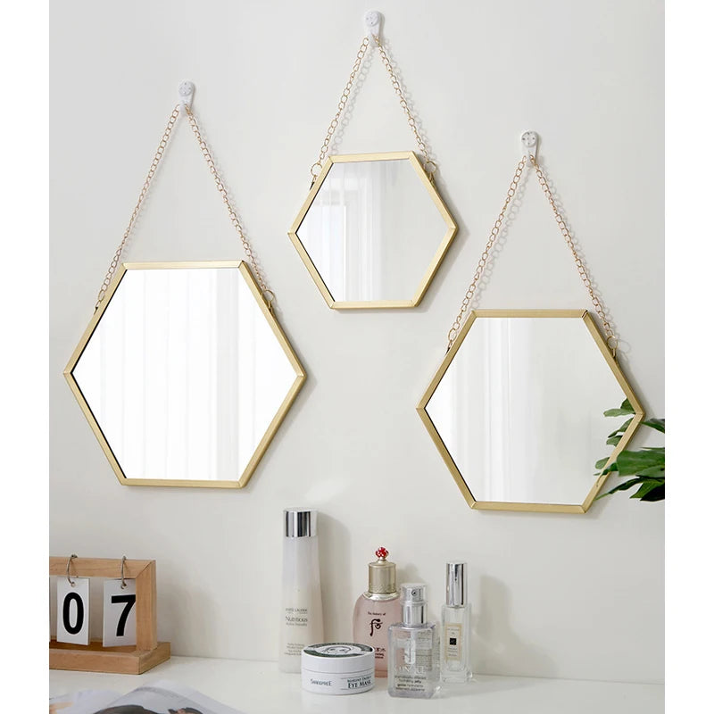 A hexagon decorative wall mirror with a gold frame and hanging on a light gray wall.