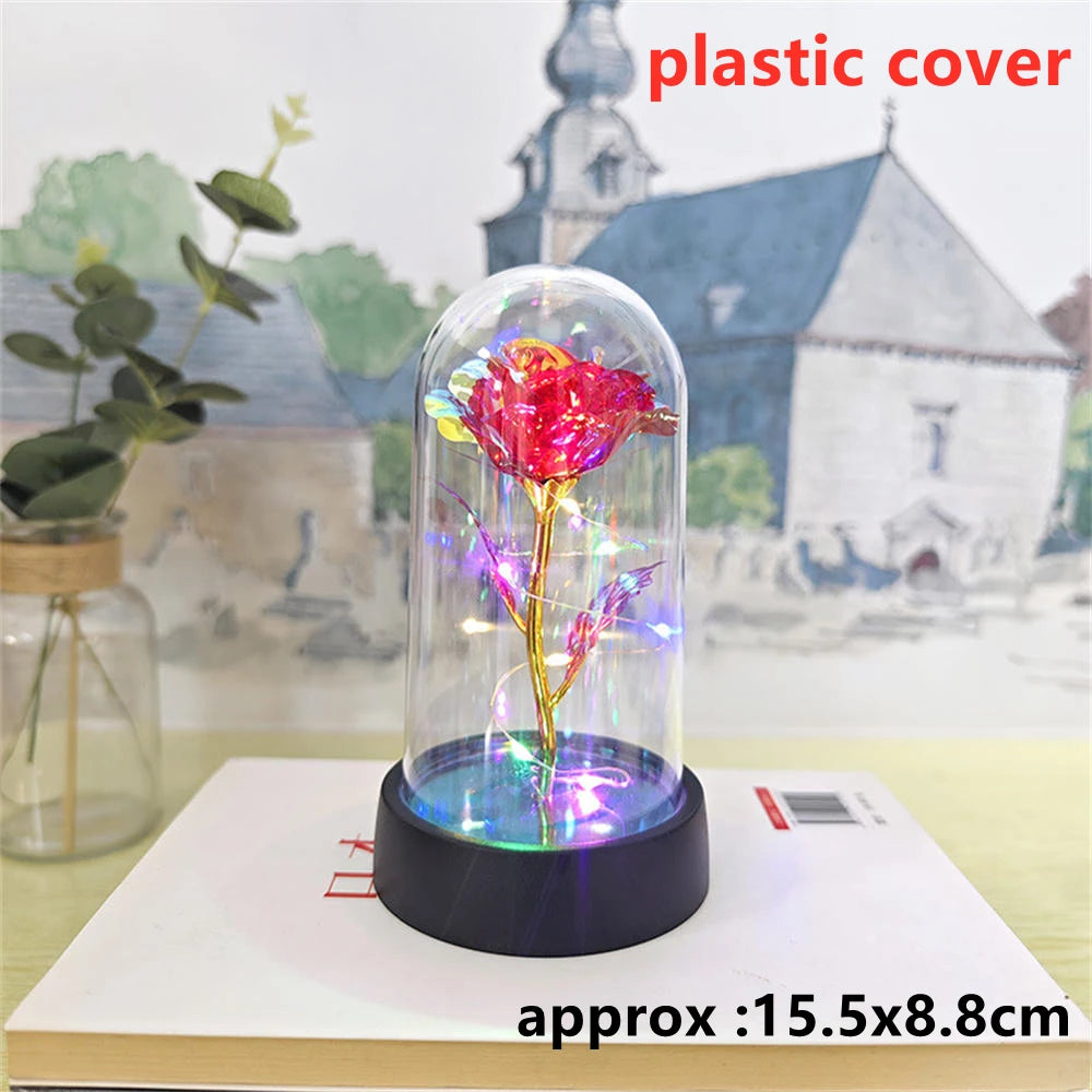 An LED galaxy rose artificial flower displayed inside a glass dome on a white surface.