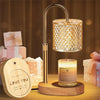 A modern adjustable heat candle warmer lamp with a brass finish sits on a wooden base.