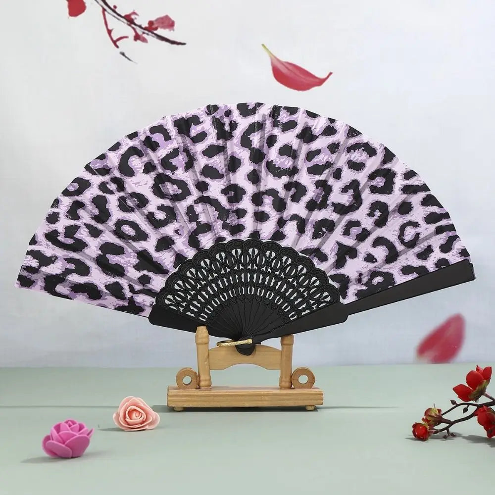 A folding hand fan with a leopard print design and black handle is displayed against a light background.