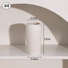A white, ribbed ceramic vase is displayed on a shelf with shadows cast by natural light.