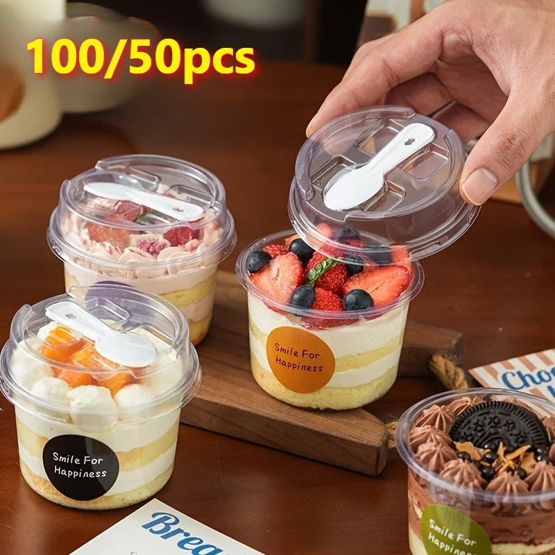 A hand holds a clear reusable pudding cup filled with layered dessert, next to other cups and a wooden board.