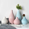 A grouping of elegant ceramic flower vases in pink and blue tones on a white surface.