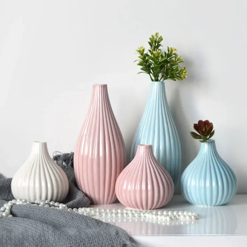 A grouping of elegant ceramic flower vases in pink and blue tones on a white surface.