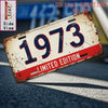 A distressed vintage metal tin sign with the number 1973 is shown in a side view on a dark surface.