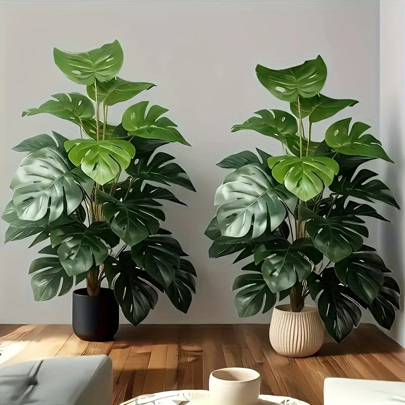 A pair of realistic artificial monstera palm trees in various shades of green displayed on a wooden surface.