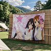 A large tapestry featuring two anime characters from K-On! in pink and white tones displayed outdoors.