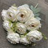 A bouquet of nine realistic white silk roses with green leaves arranged on a gray fabric.