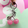 A silver keychain featuring a pink glitter cherry charm attached to a bag pendant.