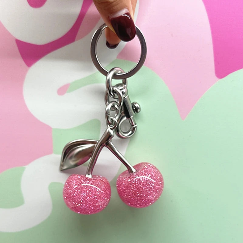 A silver keychain featuring a pink glitter cherry charm attached to a bag pendant.