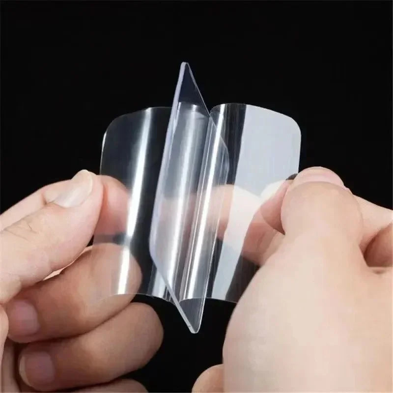 A hand is holding a clear double-sided adhesive tape, showing its transparent and flexible nature.