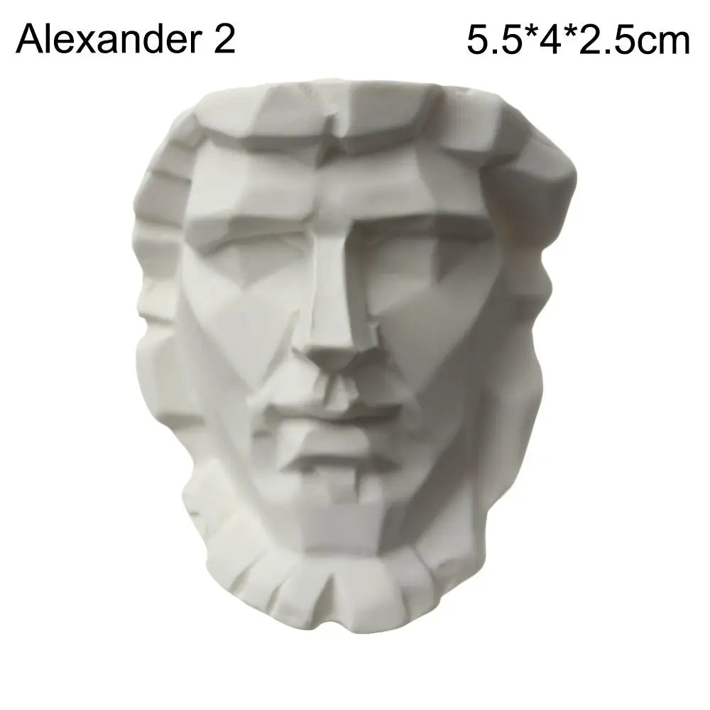 A white plaster bust miniature of a male face in the style of classical Greek mythology.