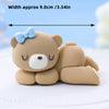 A cute, light brown cartoon elephant cake topper with a blue bow, shown lying on a white surface.