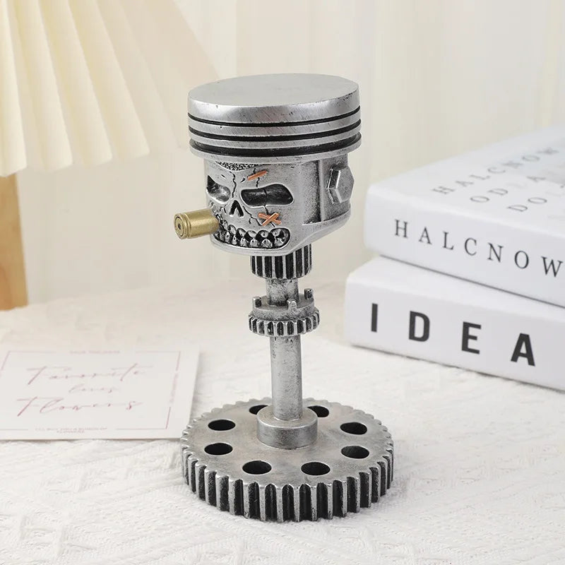 A silver mechanical piston skull sculpture with a gear base resting on a white surface.