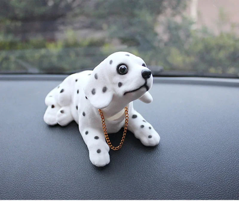 A white ceramic dog ornament with black spots and a gold chain is displayed on a dark surface.