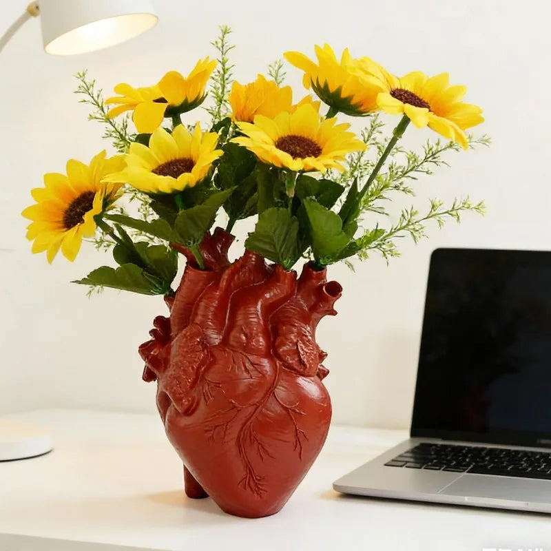 A vibrant bouquet of yellow sunflowers in a heart-shaped terracotta vase on a white table.