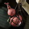 A traditional ceramic wine gourd with a narrow neck is suspended by dark cords.