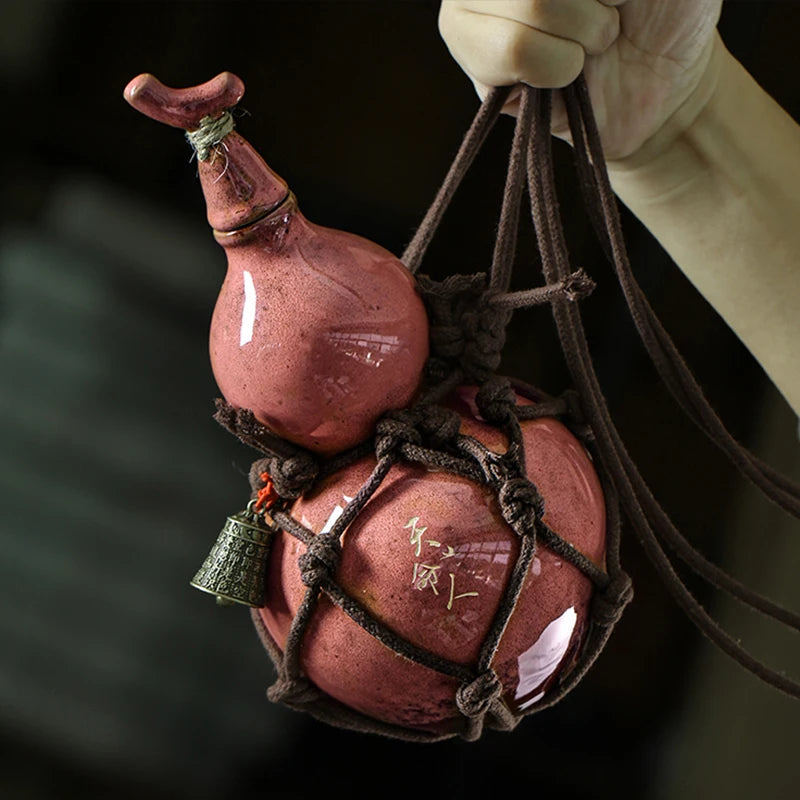 A traditional ceramic wine gourd with a narrow neck is suspended by dark cords.
