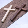 Handcrafted wooden wall cross with a two-tone finish resting on a dark wood plank.