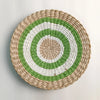 Round woven straw wall decor featuring concentric rings of natural beige, white, and green.