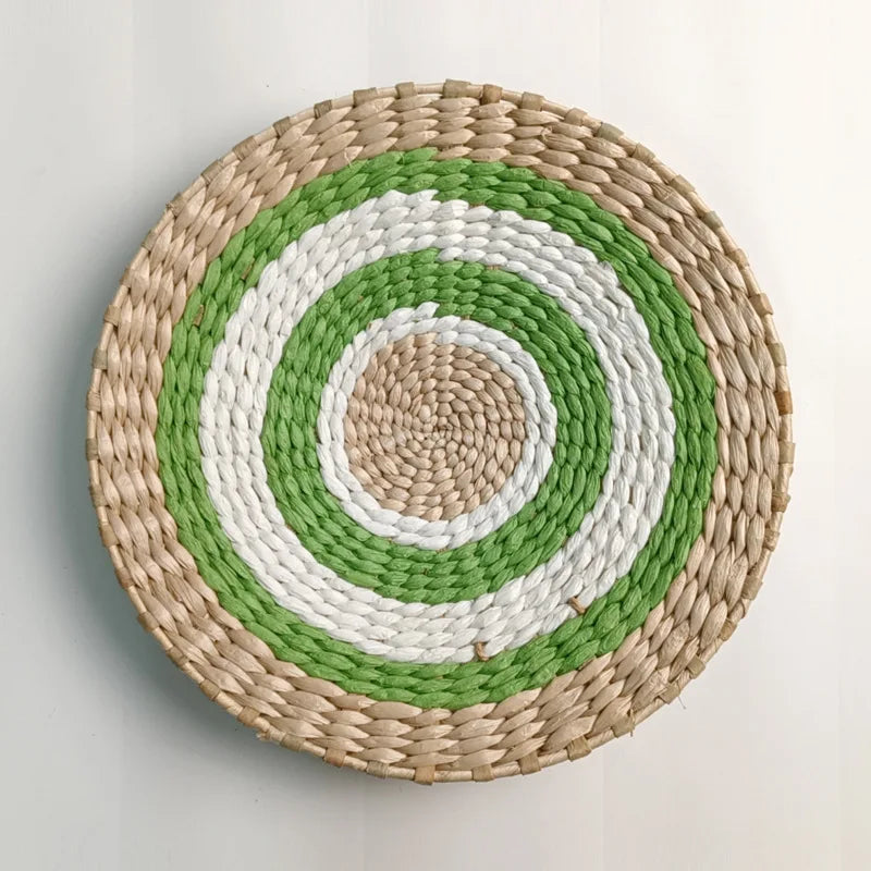Round woven straw wall decor featuring concentric rings of natural beige, white, and green.