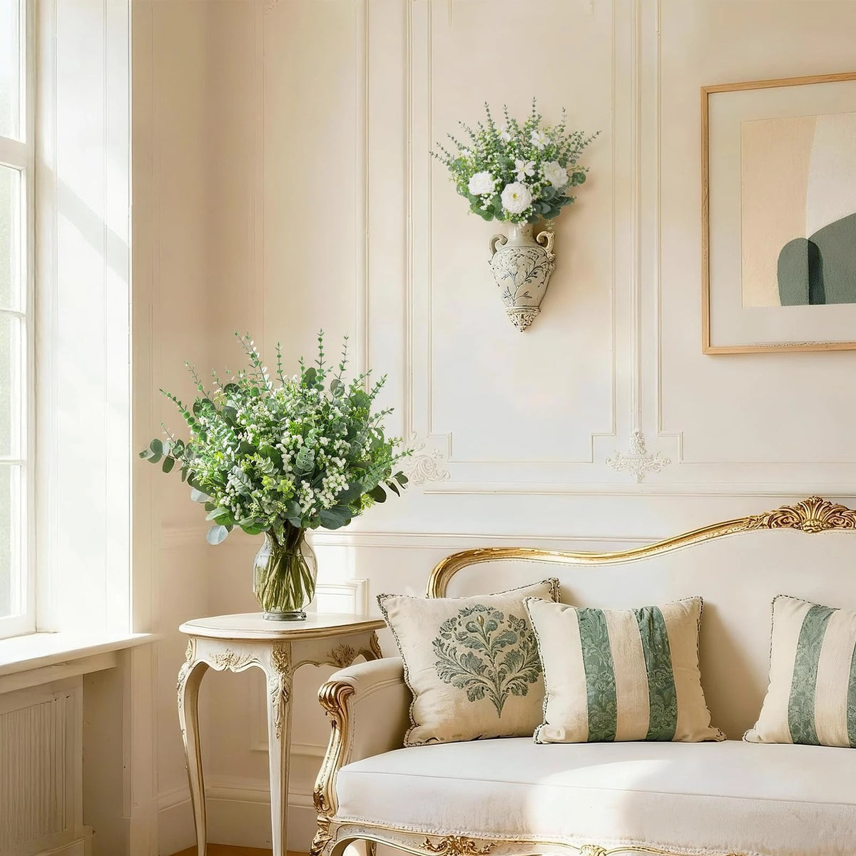 Sofá de color claro decorado con cojines y un jarrón de ramas de eucalipto verde en una habitación luminosa.