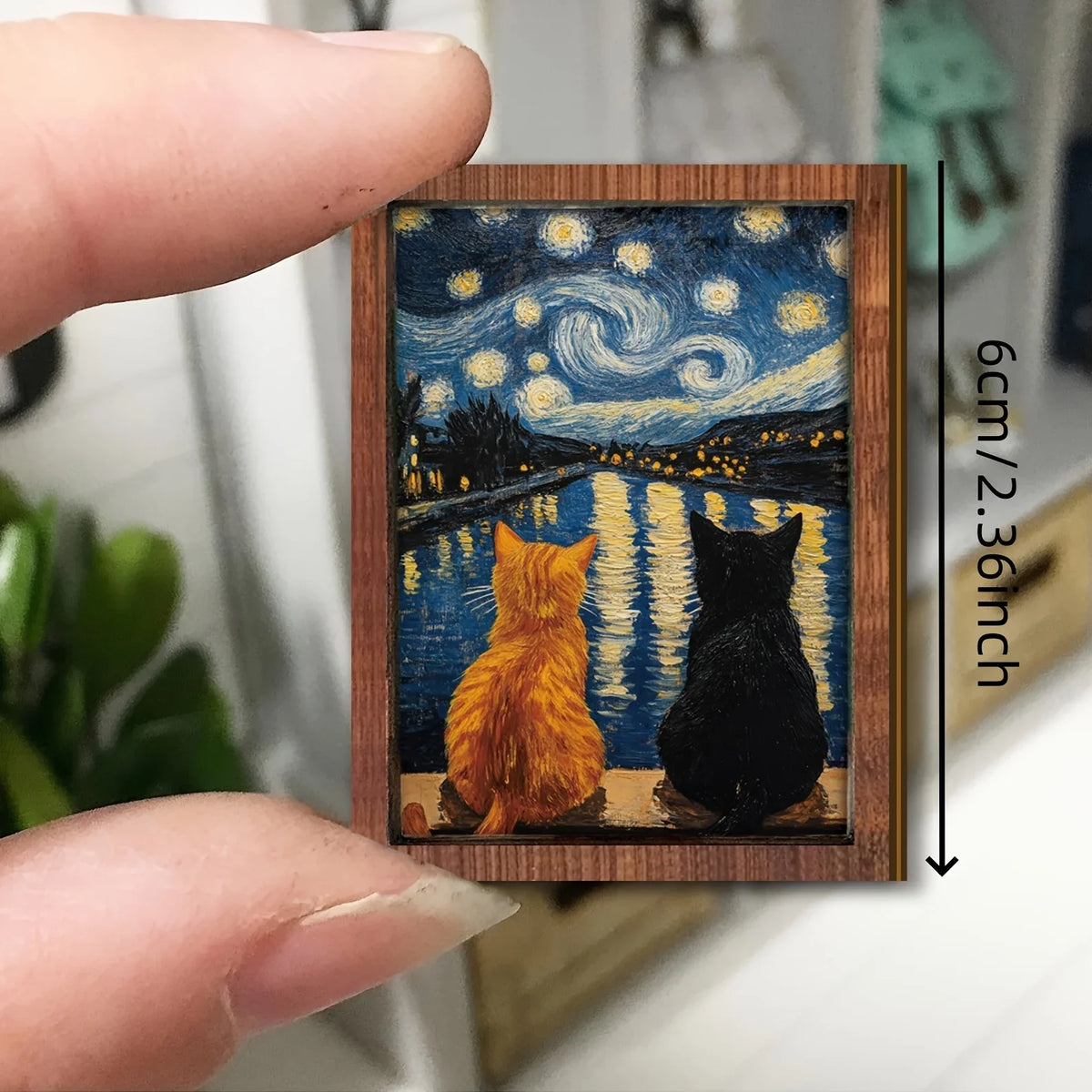 A small wooden art print featuring a starry night sky and two cats silhouetted against the water.