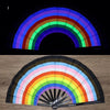 A folding fan with a rainbow color gradient displayed against a black background and on a wooden surface.