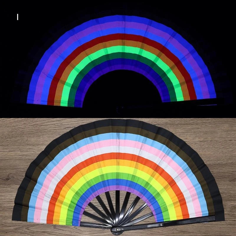 A folding fan with a rainbow color gradient displayed against a black background and on a wooden surface.