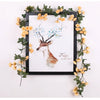A framed watercolor painting of a deer with blue blossoms surrounded by a silk rose vine garland.